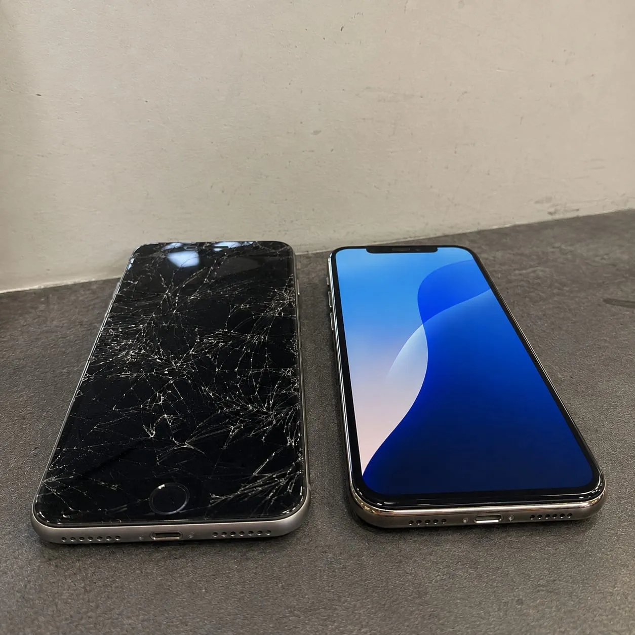 A cracked iPhone beside a freshly repaired phone on the repair bench